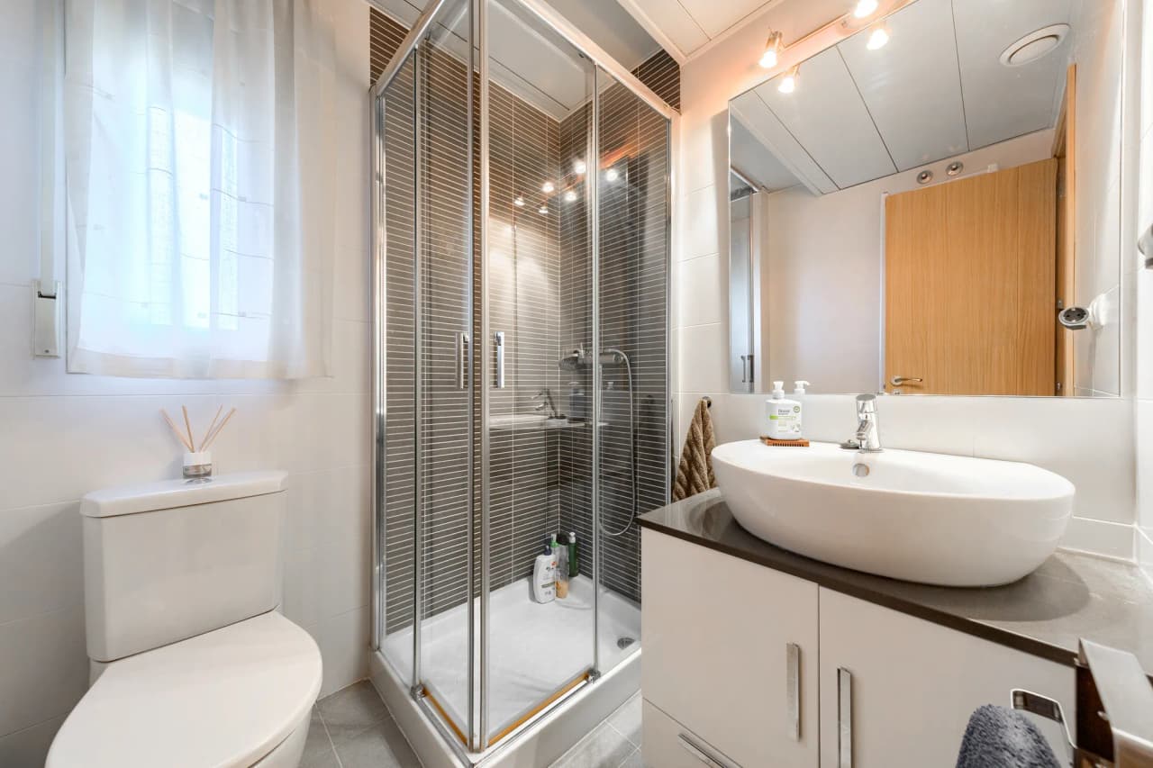 Baño con plato de ducha, mampara y lavabo sobre encimera