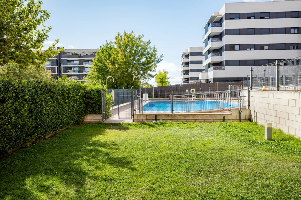 Zona ajardinada con césped natural y la piscina al fondo