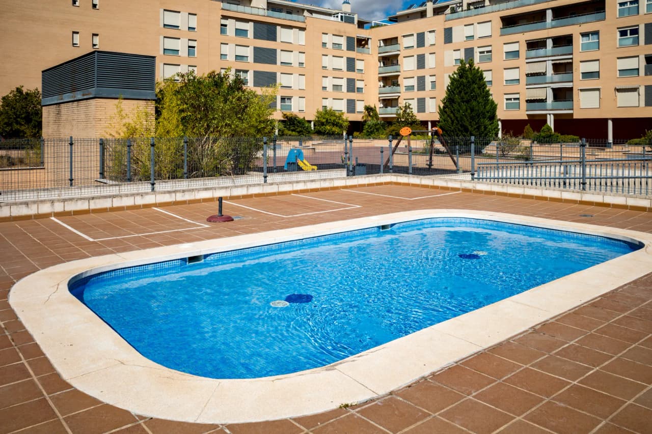 Piscina de la urbanización, con la zona de juegos infantiles al fondo