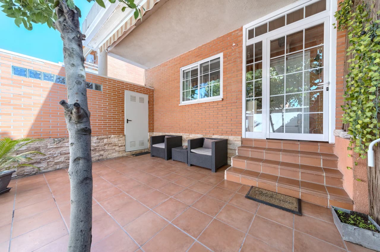 Patio de entrada con árbol, zona de estar y escalera a la puerta de la casa